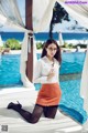 A woman in a white shirt and orange skirt posing by a pool.