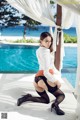 A woman in a white shirt and black stockings posing by a pool.