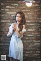 A woman in a white dress standing in front of a brick wall.