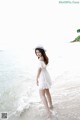 A woman in a white dress and hat standing in the water.