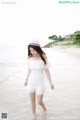 A woman in a white dress and hat walking on the beach.