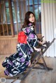 A woman in a kimono sitting on a wooden chair.