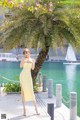 A woman in a yellow dress standing next to a palm tree.