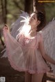 A woman in a pink dress with white wings in the woods.