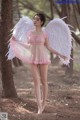 A woman in a pink dress with white wings in the woods.