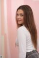 A woman with long brown hair standing in front of a pink wall.