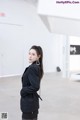 A woman in a black suit standing in a white room.