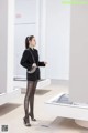 A woman in a black suit standing in front of a white wall.