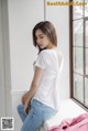 A woman sitting on a window sill wearing a white shirt and jeans.