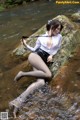 A woman in a white shirt and black skirt sitting on a rock in the water.