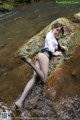 A woman in a white shirt and black skirt is sitting on a rock in the water.