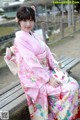 A woman in a pink kimono sitting on a bench.