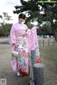 A woman in a pink kimono standing next to a fence.