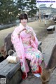 A woman in a pink kimono sitting on a bench next to a deer.