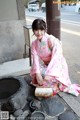 A woman in a pink kimono sitting on the ground.