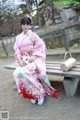 A woman in a pink kimono sitting on a bench.