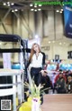 A woman standing next to a car on display at a car show.