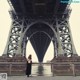 A woman standing under a bridge on a cloudy day.