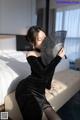 A woman in a black dress sitting on a bed holding a fan.