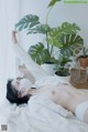 A naked woman laying on a bed next to a plant.