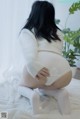 A woman in a white sweater and white stockings crouching on a bed.