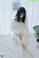 A woman sitting on a bed wearing a white sweater and white socks.