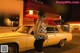 A woman standing in front of a yellow car at night.