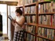 A woman standing in front of a bookshelf holding a book.