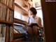 A woman sitting on the floor in front of a book shelf.