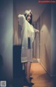 A woman in a white raincoat standing in a hallway.