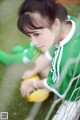 A woman in a green and white soccer uniform sitting on the ground.