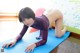 A woman in a purple bodysuit is doing yoga on a blue mat.