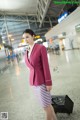 A woman in a pink jacket and skirt holding a black suitcase.