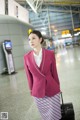 A woman in a pink suit with a suitcase in an airport.