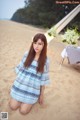 A woman sitting on the sand in a blue dress.