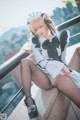 A woman in a maid outfit sitting on a ledge.