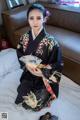 A woman in a kimono sitting on a bed holding a fan.