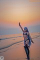 A woman in a bikini standing on a beach at sunset.