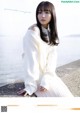 A woman in a white dress sitting on a rock by the water.