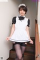 A woman in a maid outfit is posing on the stairs.