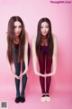 Two young women standing next to each other on a pink background.