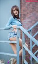 A woman in a blue shirt and denim shorts leaning against a railing.