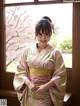 A woman in a kimono standing in front of a window.