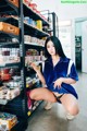 A woman in a blue shirt and black panties crouching down in a store.