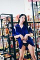 A woman in a blue shirt and black panties standing in front of a shelf of food.