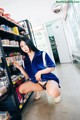 A woman in a blue shirt and black panties crouching down in a store.