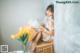 A woman sitting on top of a wooden box next to a vase of flowers.