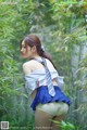 A woman in a blue skirt and a white shirt is standing in the woods.