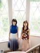 Two young women standing next to each other in front of a window.