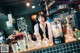 A woman behind a bar with bottles of alcohol on the counter.